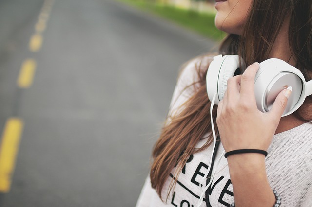 Close up of the side of a teenage girl with long dark hair and white headphones round her neck. there is a road in the back ground.