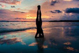 silhouette of a woman doing a yoga headstand on a sunset beach