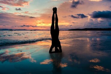 silhouette of a woman doing a yoga headstand on a sunset beach