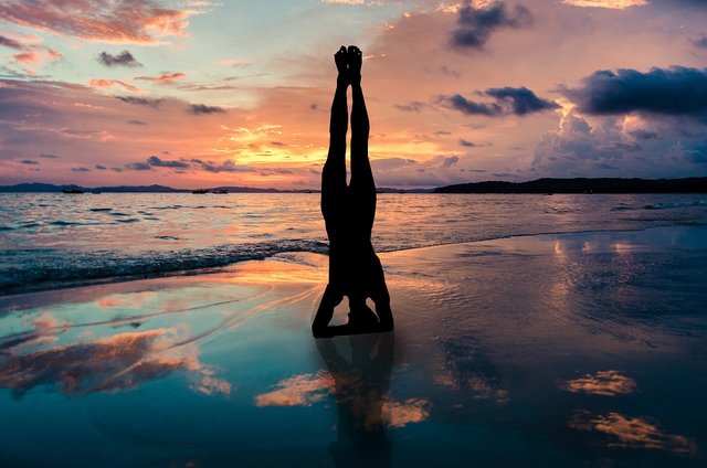 silhouette of a woman doing a yoga headstand on a sunset beach