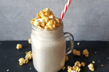 Pecan Pie smoothie in a mason jar mug topped with popcorn and a red and white striped straw