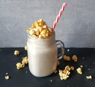 Pecan Pie smoothie in a mason jar mug topped with popcorn and a red and white striped straw