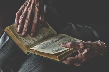 Close up of an old mans wrinkjly hands holding an open book