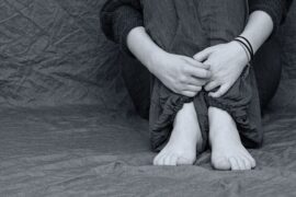 black and white image of someones hand feet and knees sat scrunched up clutching themselves