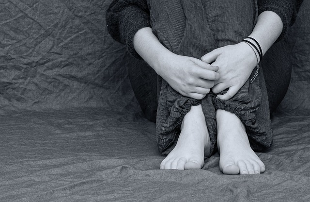 black and white image of someones hand feet and knees sat scrunched up clutching themselves