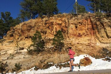 Male runner running on a road alongside a rocky embankment. There is snow at the side of the road suggesting it is cold but he has still got the motivation to get outside and exercise.