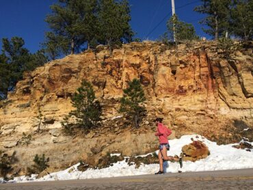 Male runner running on a road alongside a rocky embankment. There is snow at the side of the road suggesting it is cold but he has still got the motivation to get outside and exercise.