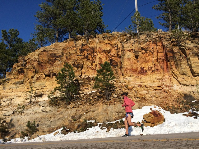 Male runner running on a road alongside a rocky embankment. There is snow at the side of the road suggesting it is cold but he has still got the motivation to get outside and exercise.