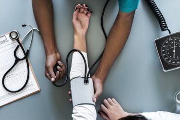 aerial photo of doctors arms taking the blood pressure of a patient