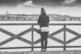blacl and white photo of a woman stoof with her back to the camera on a pier overlooking the sea.