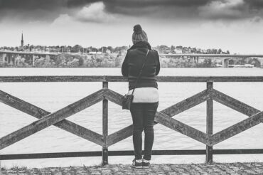 blacl and white photo of a woman stoof with her back to the camera on a pier overlooking the sea.