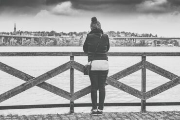 blacl and white photo of a woman stoof with her back to the camera on a pier overlooking the sea.