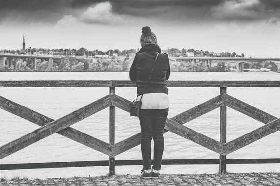 blacl and white photo of a woman stoof with her back to the camera on a pier overlooking the sea.