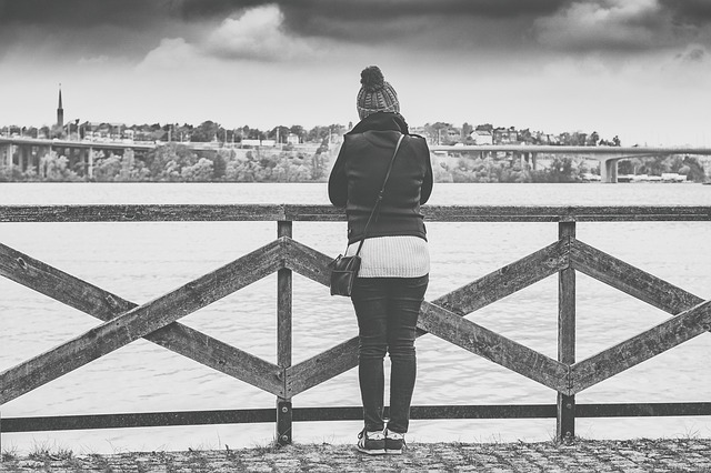 blacl and white photo of a woman stoof with her back to the camera on a pier overlooking the sea.