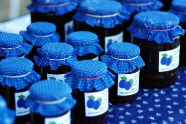 rows of organic plum jam in jars with purple cloth lids and hand printed labels