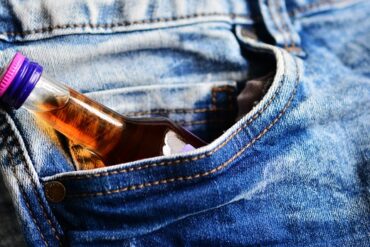 small bottle of brandy poking out of the pocket of a pair of blue jeans suggesting the person had addiction issues