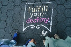 looking down to a dark tiled floor on which the words fulfill your destiny have been written in yellow and pink chalk