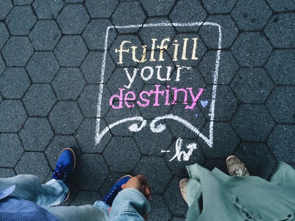 looking down to a dark tiled floor on which the words fulfill your destiny have been written in yellow and pink chalk