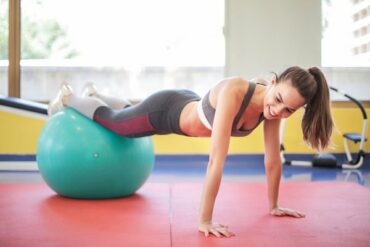 Young woman in gym kit doing a press up while her legs are resting on a green exercise ball
