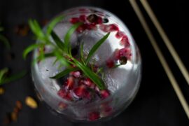 Photo taken from above looking down on a gin cocktail decorated with a herb sprig and pomegranite seeds