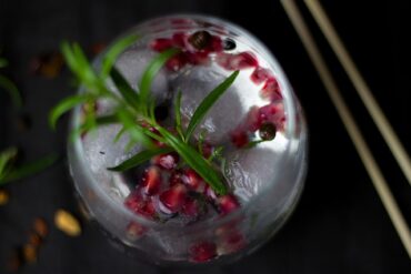 Photo taken from above looking down on a gin cocktail decorated with a herb sprig and pomegranite seeds