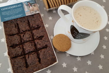 Horsham gingerbread in it's tray packet with a mug of cappucino on a plate and some biscuits