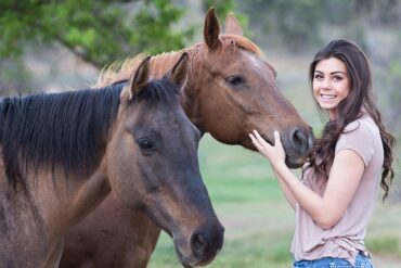brunette girl in her twenties stood next to two brown horses