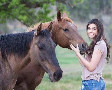 brunette girl in her twenties stood next to two brown horses