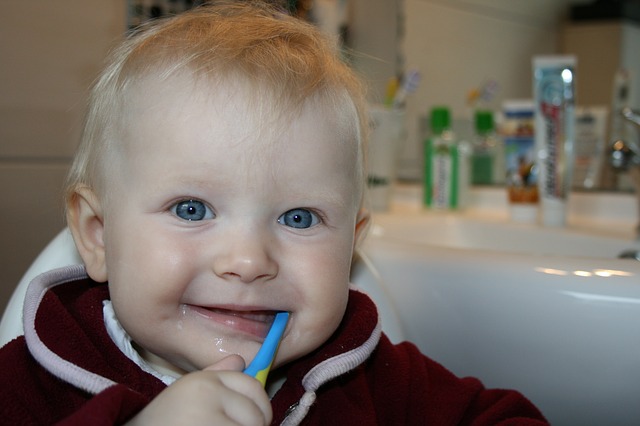 Toddler chewing on a blue toothbrush in a bathroom