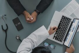 aerial photo of a doctor and his patient. you can just see their arms and the doctor is using a laptop to map out the patient journey