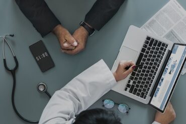 aerial photo of a doctor and his patient. you can just see their arms and the doctor is using a laptop to map out the patient journey