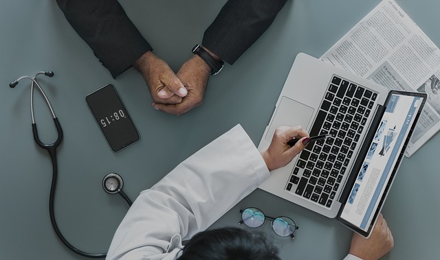 aerial photo of a doctor and his patient. you can just see their arms and the doctor is using a laptop to map out the patient journey