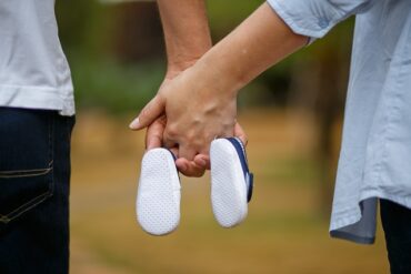 man and woman holding hands with two baby shoes hanging off of their little fingers