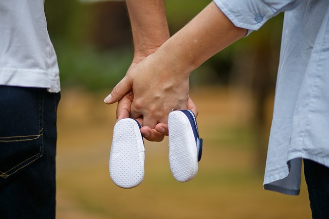 man and woman holding hands with two baby shoes hanging off of their little fingers