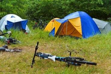 Two tents pitched in a long grass field with bikes on the ground in front of them
