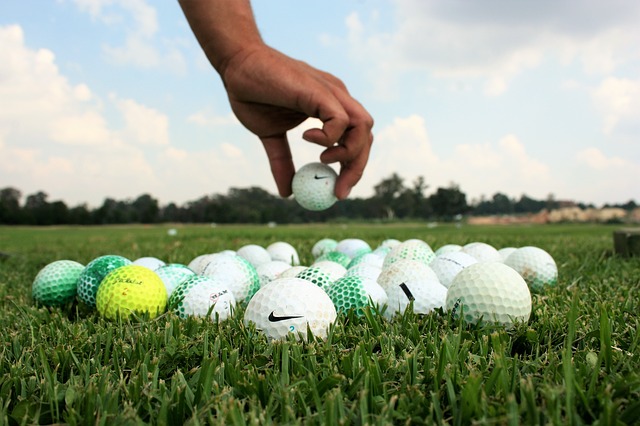 Close up of a lot of golf balls on a patch of grass with a hand reaching down to grab one