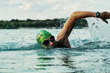 Man swimming in open water, he is wearing a green swimming hat and goggles