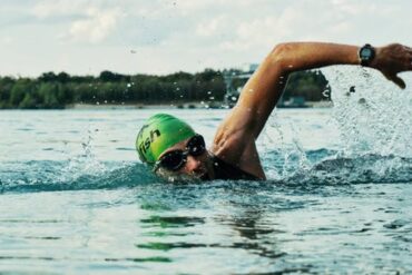 Man swimming in open water, he is wearing a green swimming hat and goggles