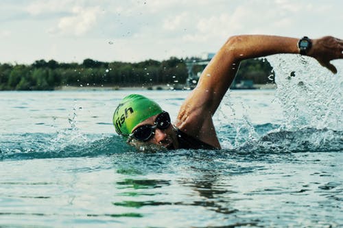 Man swimming in open water, he is wearing a green swimming hat and goggles