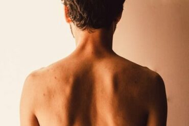 Back of a man from mid chest up. He doesn't have a top on.