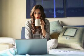 woman sat n front of an open laptop drinkng a cup of coffee and trying to take the stress out of balancing her professional and family life