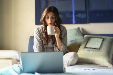 woman sat n front of an open laptop drinkng a cup of coffee and trying to take the stress out of balancing her professional and family life