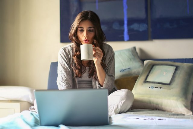 woman sat n front of an open laptop drinkng a cup of coffee and trying to take the stress out of balancing her professional and family life