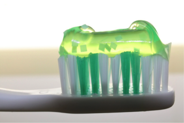 close up of the head of a white toothbrush wth a stripe of green clear toothpaste on it