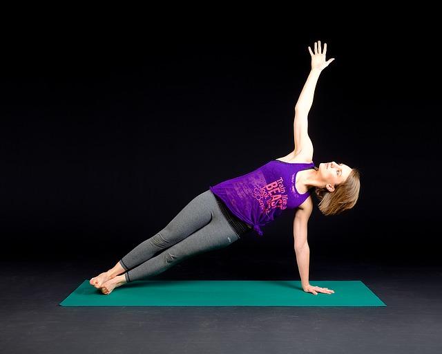 woman in workout gear doing a side plank stretch on a green exercise mat set against a plain black background