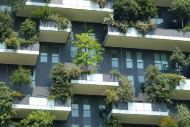 Exterior of a tall building with balconies that are filled with greenery and trees