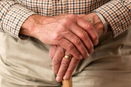 close up of an old mans hands holding thee top of a walking stikc so that you can barely see it
