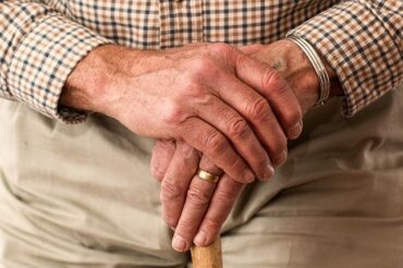 close up of an old mans hands holding thee top of a walking stikc so that you can barely see it