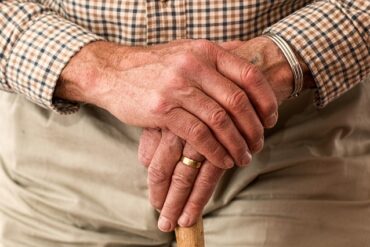 close up of an old mans hands holding thee top of a walking stikc so that you can barely see it