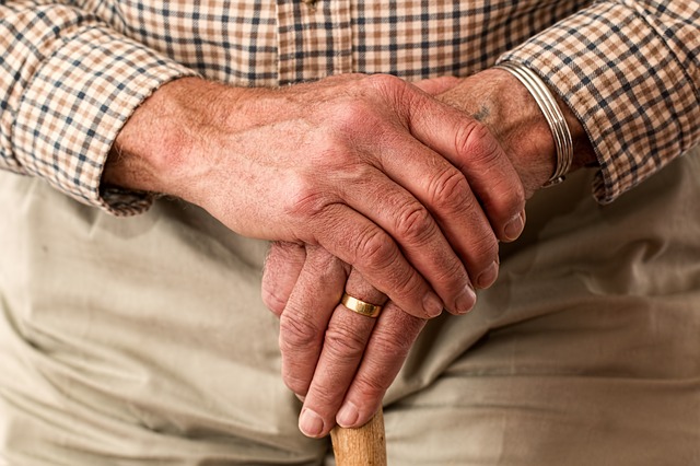 close up of an old mans hands holding thee top of a walking stikc so that you can barely see it
